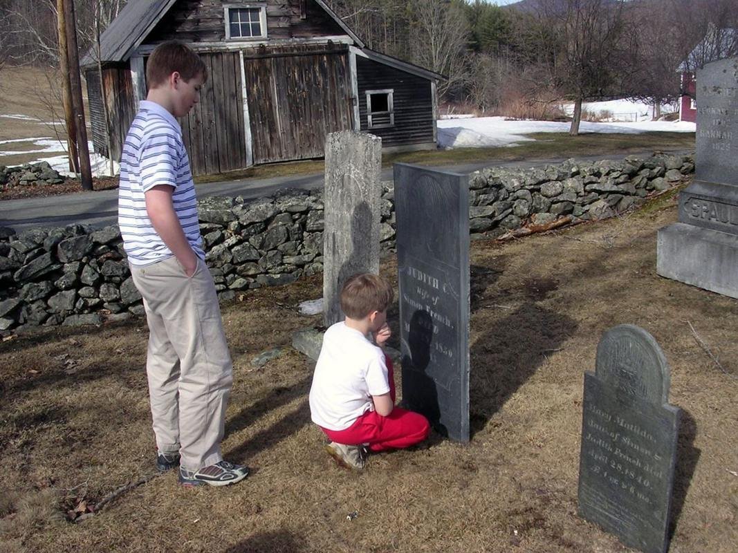 Children research 200-year old slate headstones in a local cemetery with classic New England stone walls in the background.