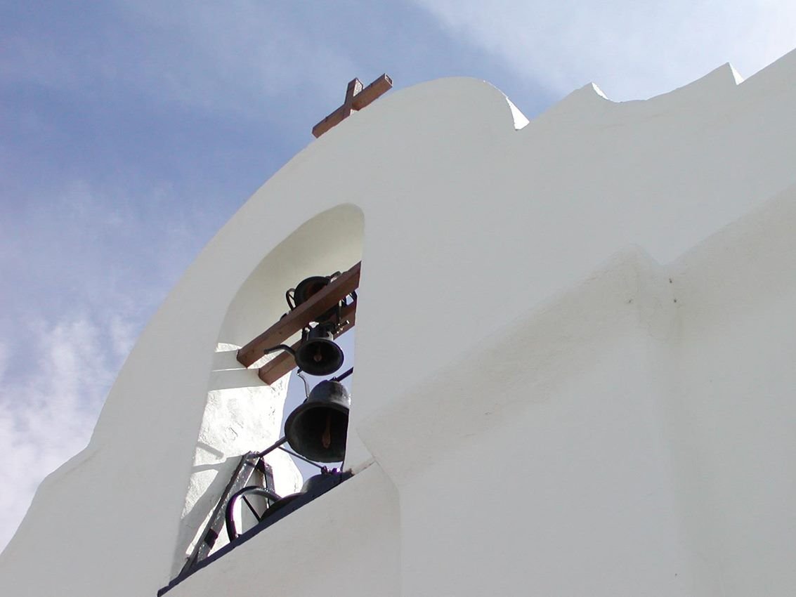 A cross and bell on the roof alcove of a white stucco church.