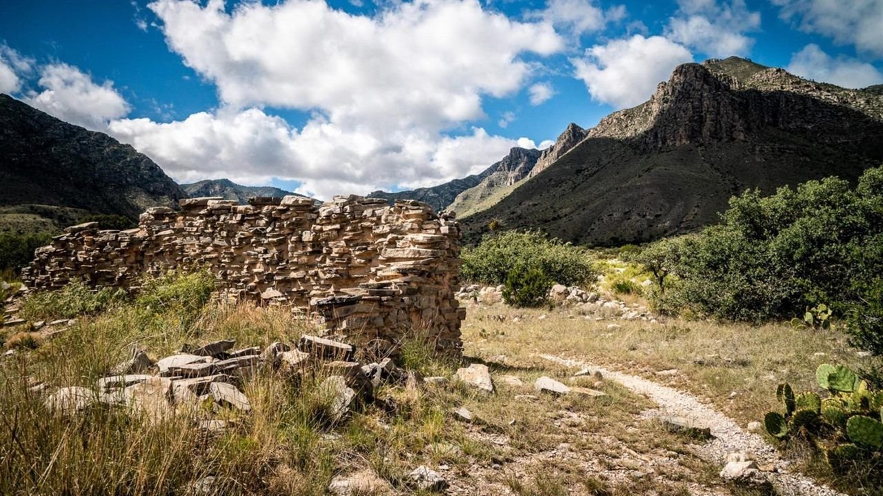 A historic stone wall stands in ruins next to a hiking trail leading into the Guadalupe Mountains NP