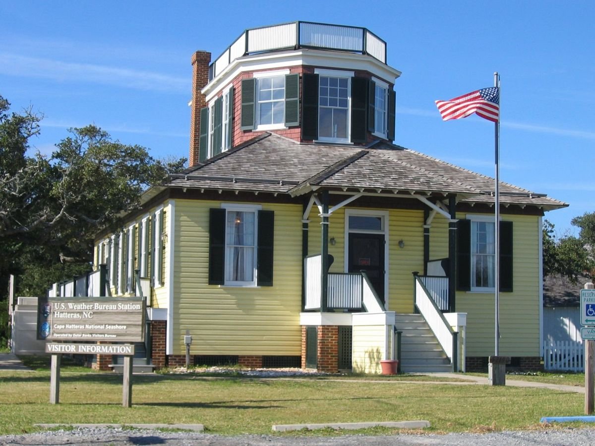 The enormous second-story railed belvedere atop the shingled hip roof of the first story of this odd-looking building along the Outer Banks Scenic Byway was the observation tower and deck for the U.S. Weather Service in 1902. Now the Hatteras Welcome Center, it has been restored to its original appearance with bright yellow clapboards on the first floor and red painted shingles visible between the dark-green shutters of the second story’s many windows.