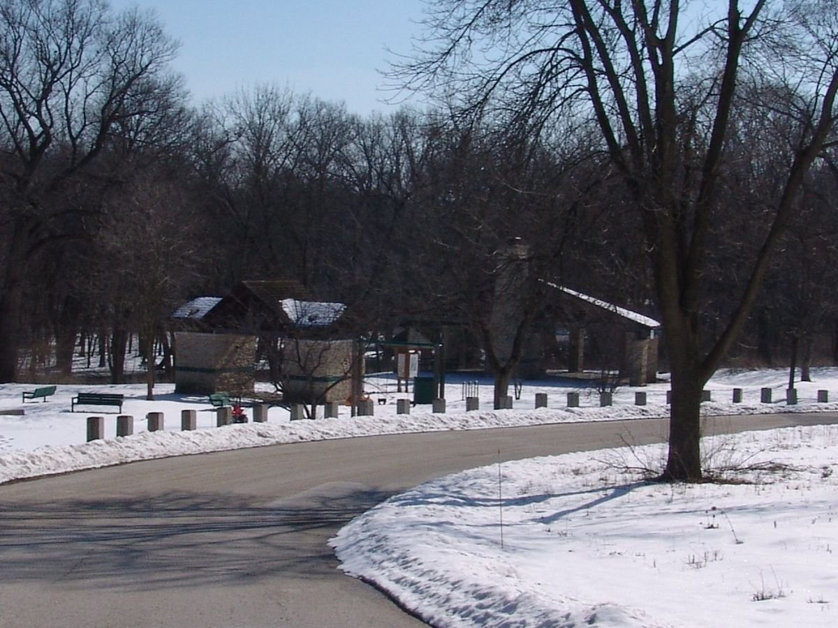 The park road curves past two park structures surrounded by snow in winter at Les Arends Forest Preserve Park near Batavia, Illinois.