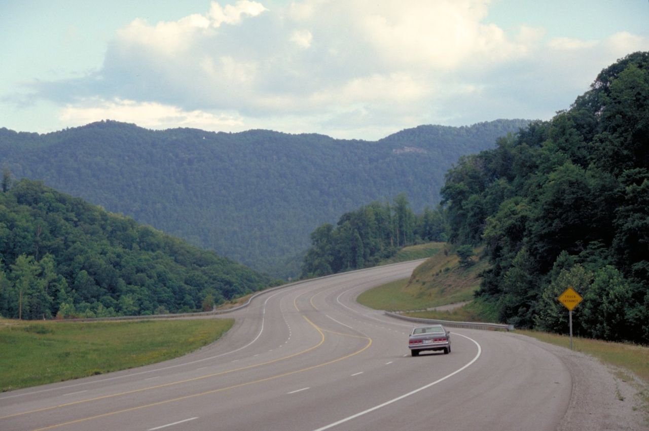 A lone driver approaches a curve through tree-covered, rounded mountains on Highway 23, the Country Music Highway, near Pikeville, Kentucky.
