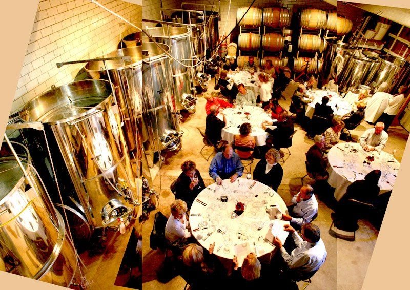 Guests savor delicious vintages in the cellar of Creekside Vineyards. They are surrounded by stainless steel tanks and stacked barrels.