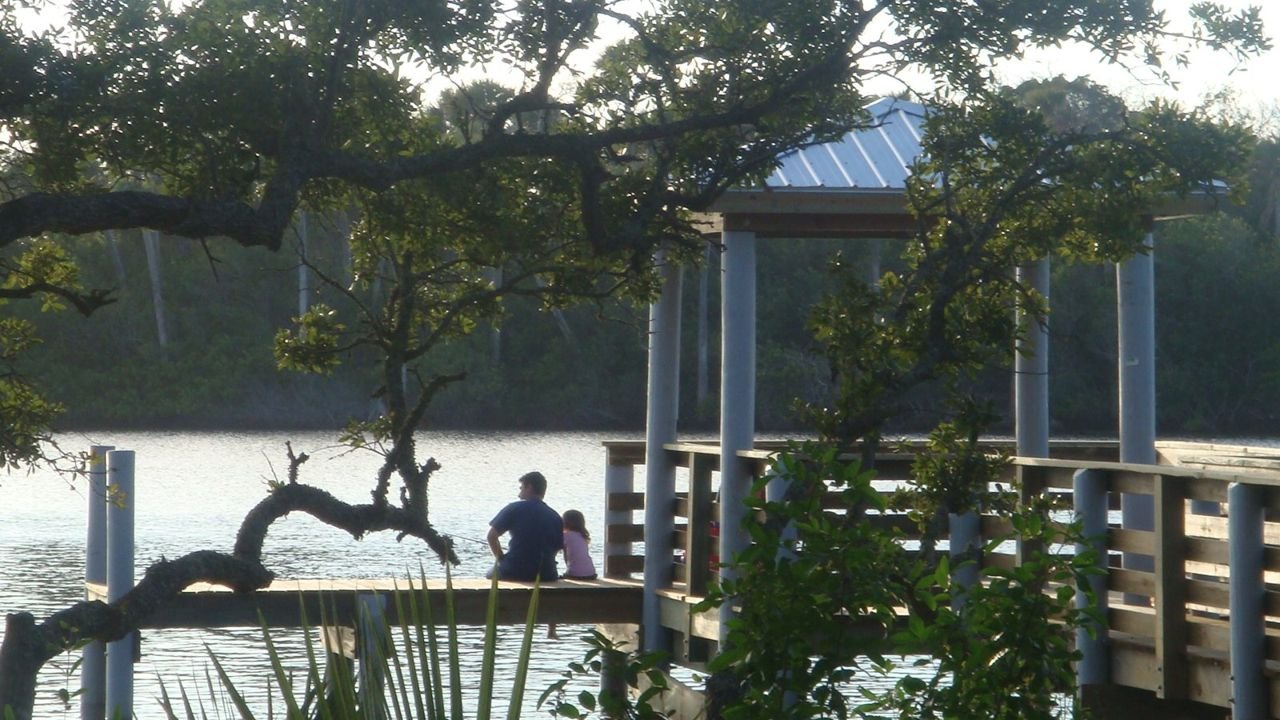 A father and his daughter sit at the dock of Seabridge Park, enjoying the calm waters and beautiful scenery.