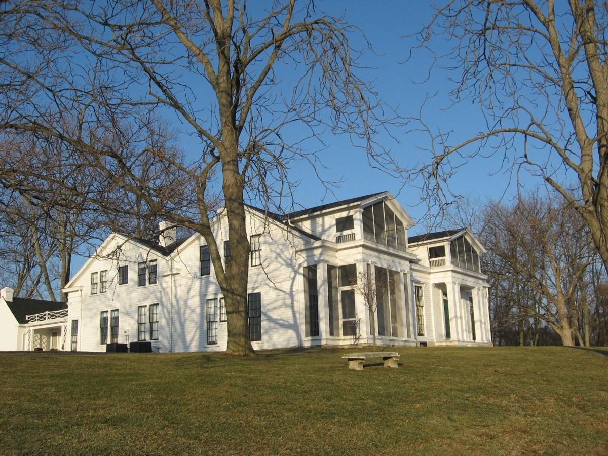 Sitting on a bluff overlooking the Ohio River, the Historic Home Veraestau is a large white house with screened-in porches on the front and is surrounded by skeletal, leafless trees.